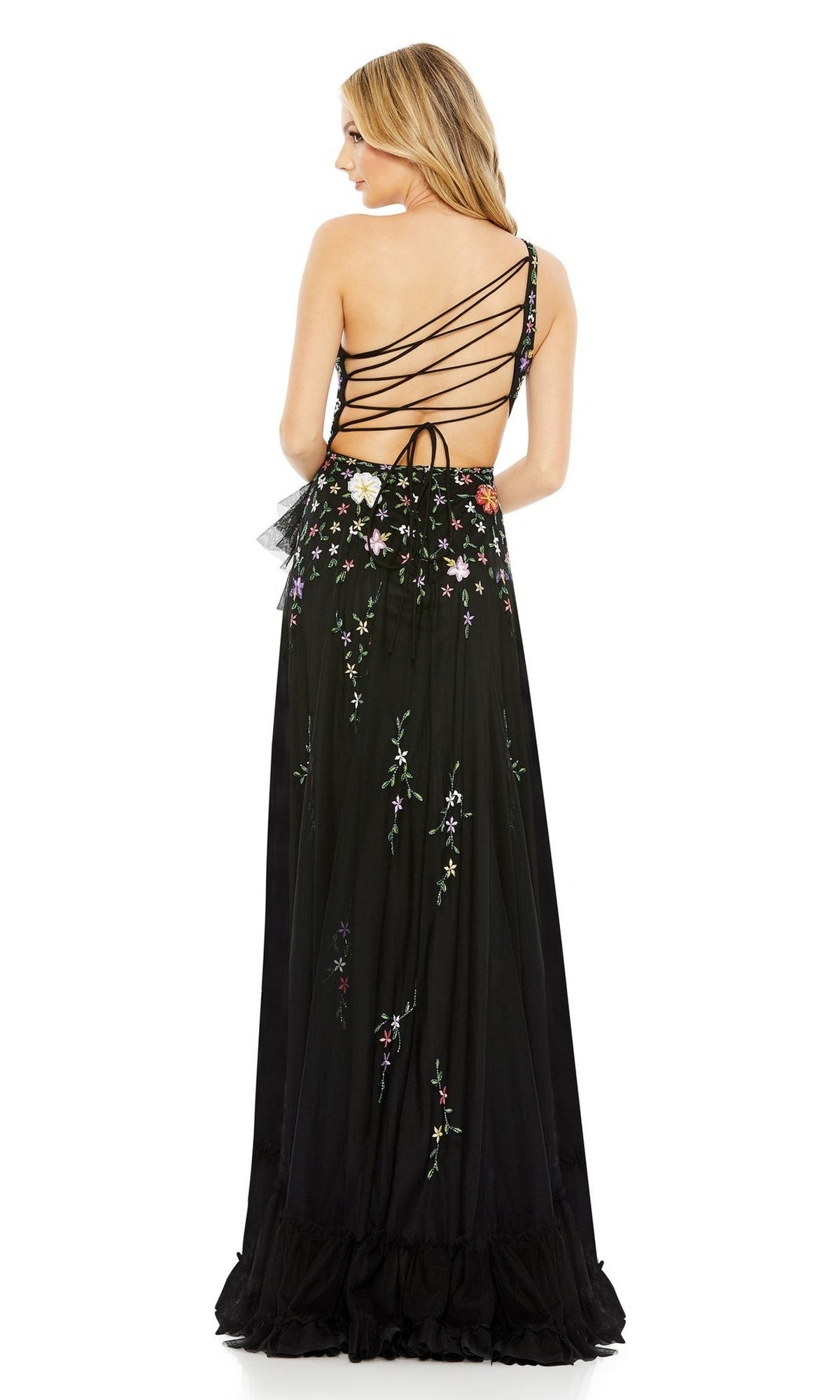 A woman faces away from the camera in the Mac Duggal 9164 One-Shoulder Floral Formal Dress, a long black gown with floral embroidery and an open back featuring crisscrossed straps.